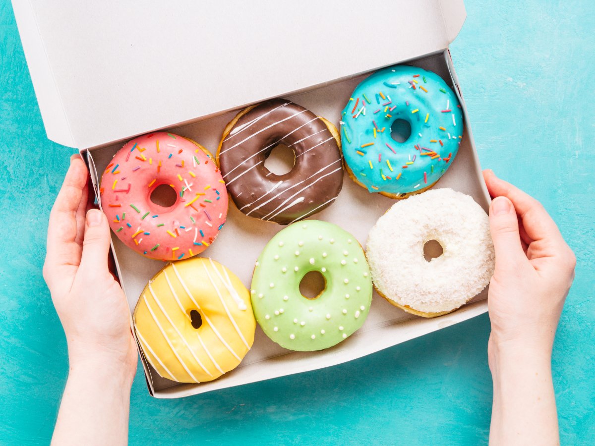 Female hands holding box with colorful donuts on blue concrete background